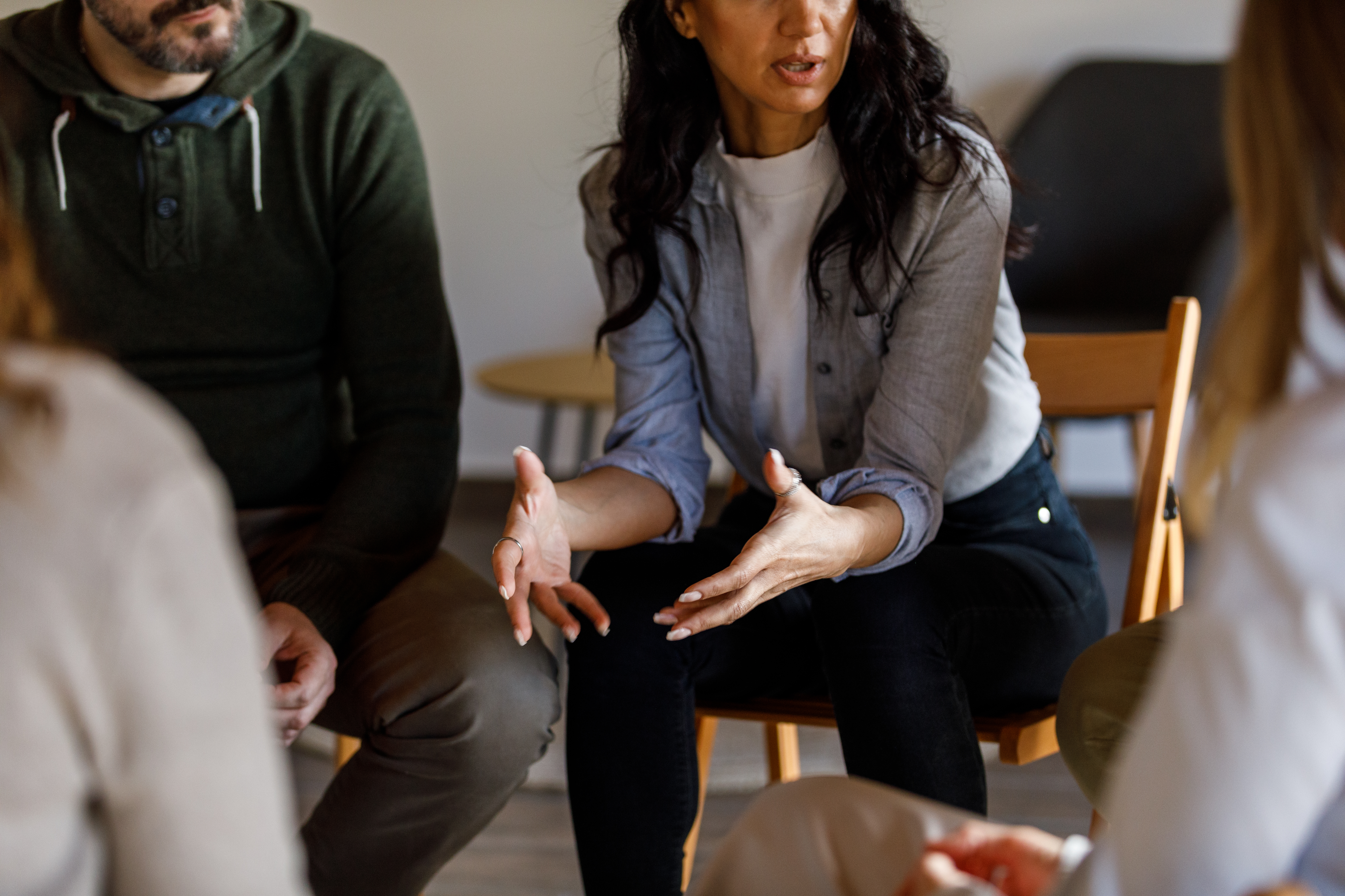 Cut out shot of anxious woman sitting in circle and talking about her mental health struggles with her peers during a group therapy session.